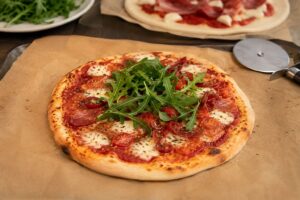 Pizza maison à la sauce tomate, mozzarella fondue et feuilles de basilic posée sur une planche en bois